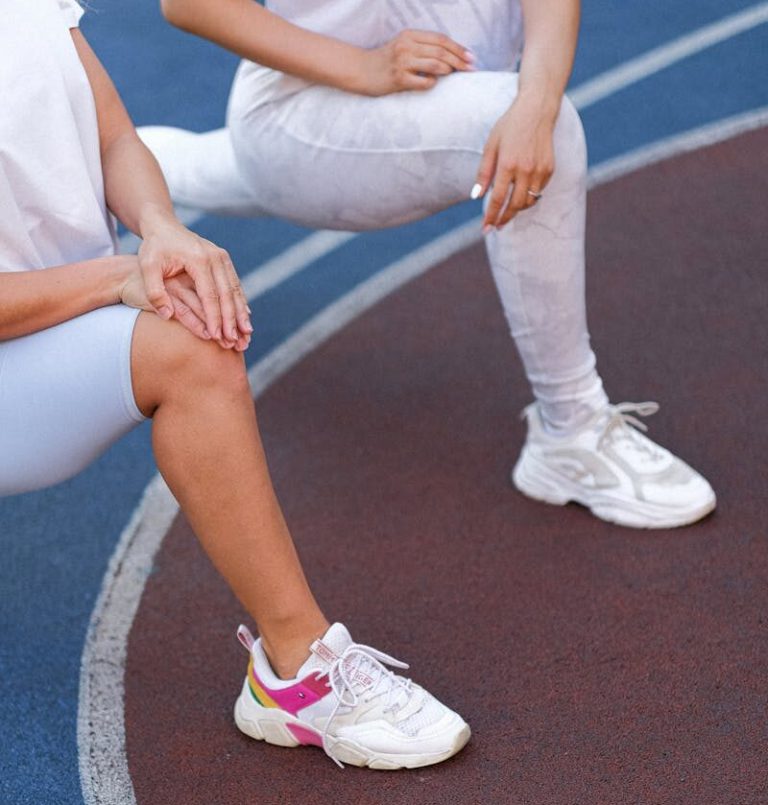 High angle of unrecognizable women in sportswear stretching legs before training on stadium